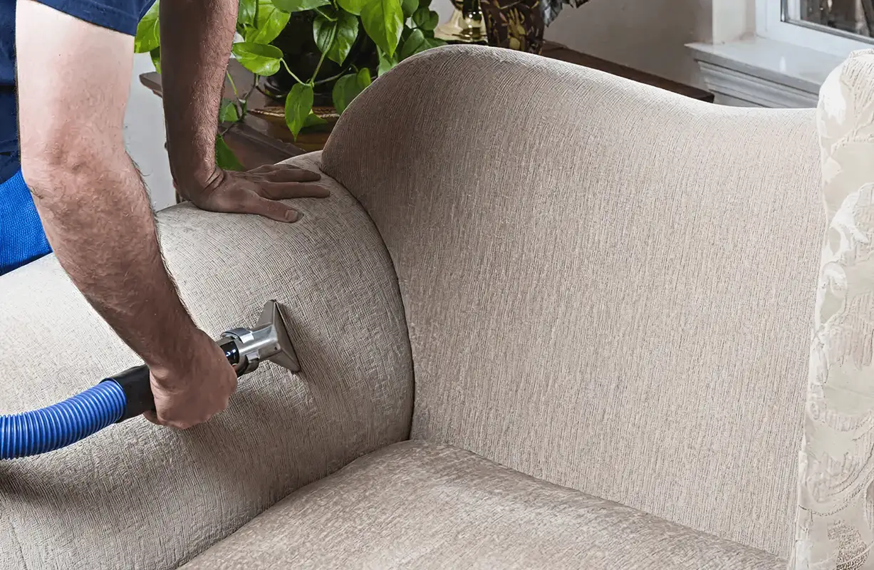 Professional upholstery cleaner deep-cleaning a fabric sofa with a handheld extraction tool and hose, Erie, PA.